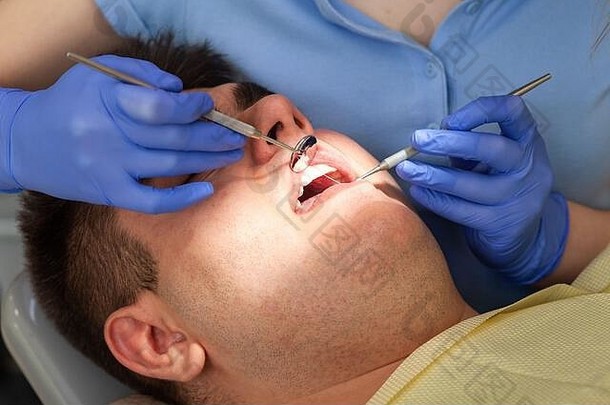 在诊所看女牙医的男人。年轻人张<strong>大嘴巴</strong>坐在牙科诊所参加年度检查。