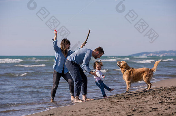 秋天，一个快乐的小家庭和孩子们在海滩上玩狗和风筝
