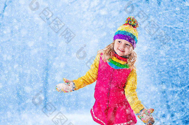 穿着粉色夹克和彩色针织帽子的小女孩在冬季公园捕捉雪花。孩子们在雪林中户外玩耍
