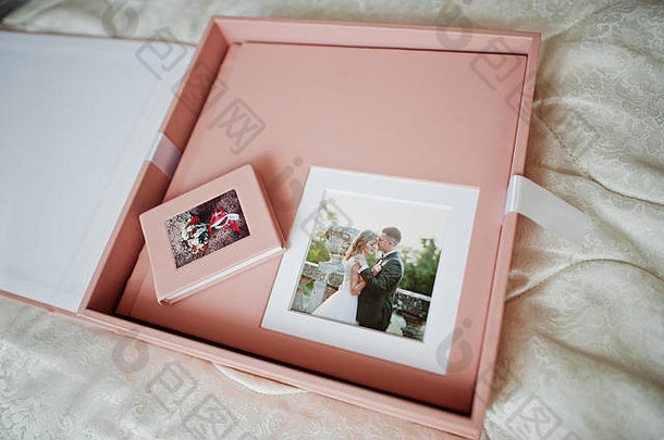 床上放着柔和的粉红色婚礼相册或相册、盒子和cd盒。