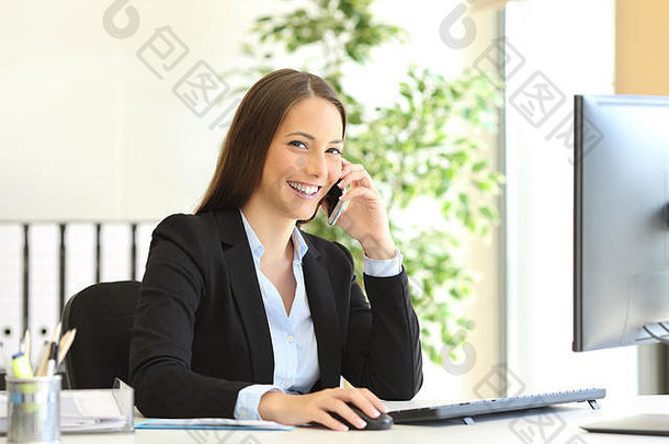 一位快乐的高管穿着西装打电话给客户服务部，看着坐在办公室办公桌上的摄像机