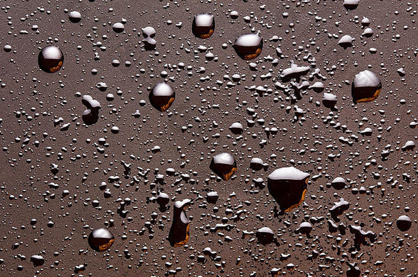 亮晶晶的水滴落在深褐色阴郁的表面上。抽象背景，俯视特写。