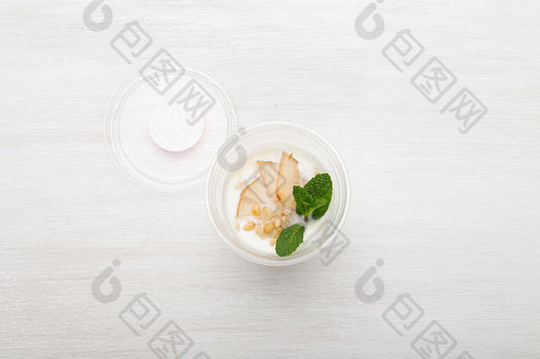 酸奶梨片、薄荷和松子放在白桌子上的午餐盒里，旁边散落着松子和梨片。健康饮食观念