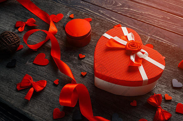 心形礼品盒，木质背景上有毡心和缎带。用礼物、礼品盒、红心组成。