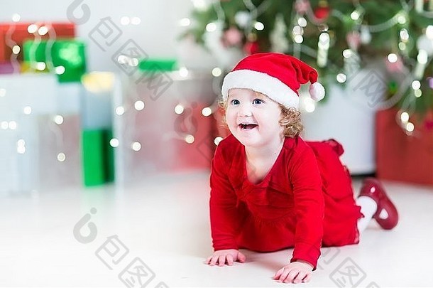 在装饰过的圣诞树旁，穿着红色连衣裙、戴着圣诞帽的快乐在五颜六色的圣诞礼物之间嬉戏