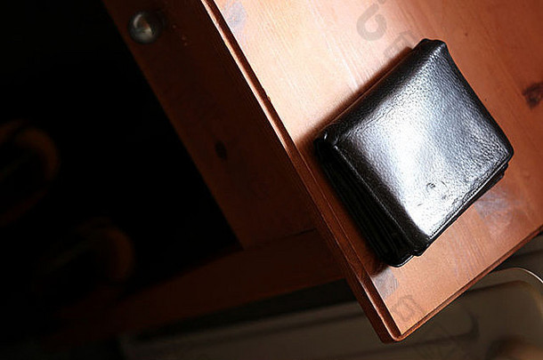 一个黑色皮革钱包躺在木制床头柜上的特写镜头