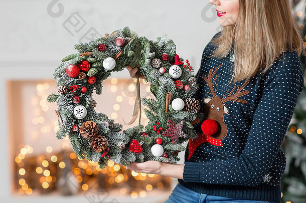 年轻女子手持圣诞花环和枞树枝作为节日礼物。新年庆典。在壁炉和圣诞树、灯光、花环的背景上