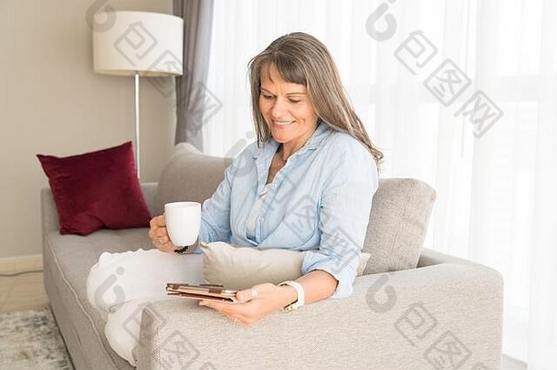 一个成熟的女人在她的城市公寓里看着平板电脑屏幕