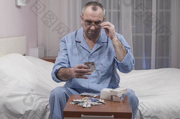 生病的老人坐在床上，选择药物和药片。