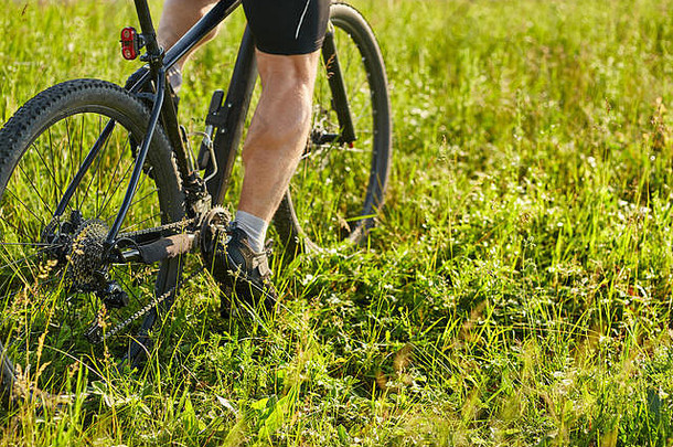 特写镜头骑自行车的人男人。腿骑山自行车绿色草地