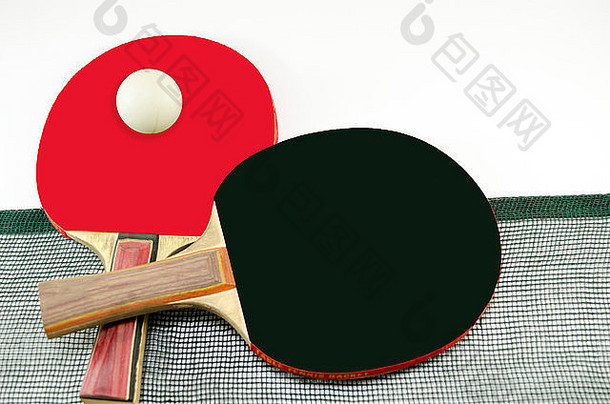 两个乒乓球拍，一个在另一个上面，一个旧的网被隔离在白色的地板上。一个桨是<strong>红色</strong>的，另一个是黑色的