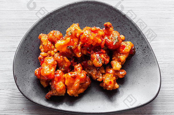 中式<strong>韩国料理</strong>-黑色盘子上的Kkanpunggi辣蒜香炸鸡片和甜酱蔬菜的俯视特写