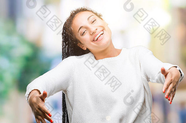年轻的辫子头发的非裔美国女孩穿着冬季毛衣，在孤立的背景下看着摄像机，张开双臂微笑着拥抱。啦啦队