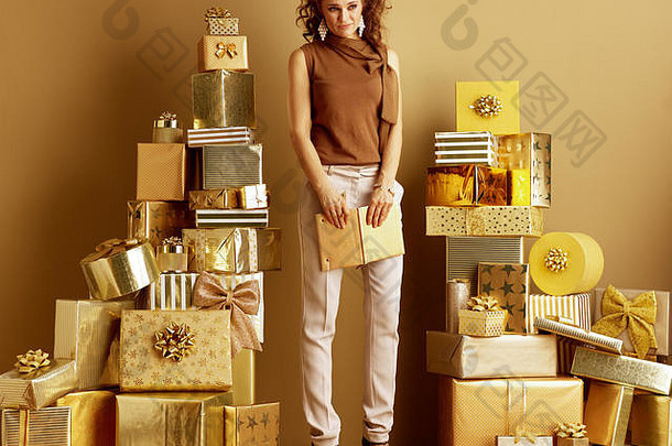 完整的长度肖像伤心时尚的购物者女人黄金米色裤子棕色（的）上衣桩金礼物前面平原墙持有
