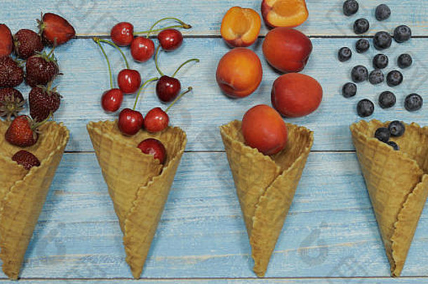 浆果和水果冰淇淋。在蓝色木质背景上，将各种新鲜水果、蓝莓、草莓、樱桃、杏平放在华夫格蛋卷中。夏季甜<strong>点菜单</strong>概念。冰淇淋制作