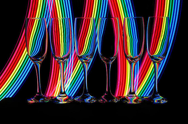 一排六个空香槟酒杯/长笛，在黑色背景上相互隔离，后面有彩色霓虹灯条纹的光画