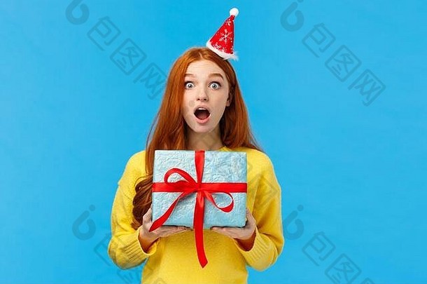 惊诧美丽的红发女孩收到意想不到的圣诞礼物送给同学，张大嘴巴惊愕而无语地盯着相机