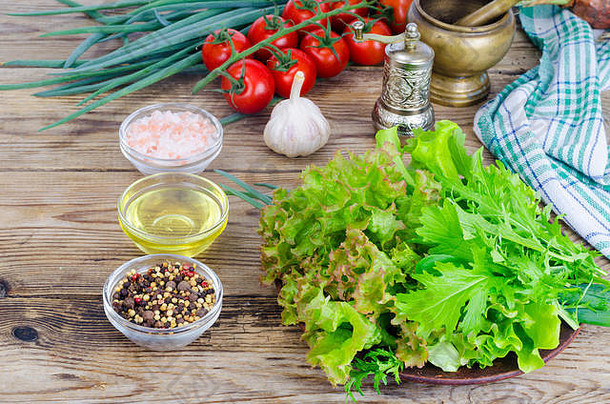 绿色沙拉成分有机生菜、樱桃西红柿、香料和橄榄油，木质背景。