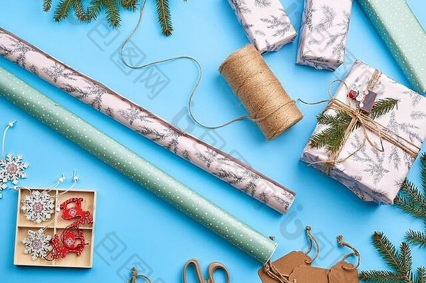 卷上包装纸、棕色绳子、剪刀、花色和一个包装好的方形盒子，还有一份礼物。DIY礼品制作流程，蓝色背景