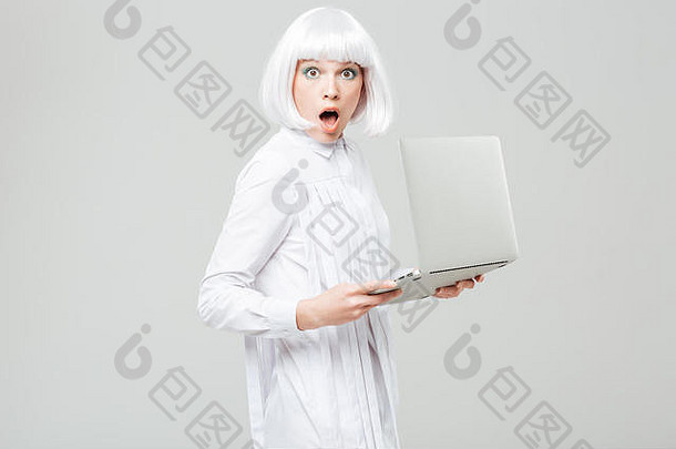 在白色背景下，一个张大嘴巴拿着笔记本电脑的漂亮女孩惊讶不已
