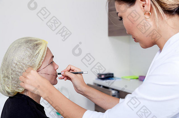 年轻的女整形外科<strong>医生</strong>在医务室做整形手术前在妇女脸上做标记