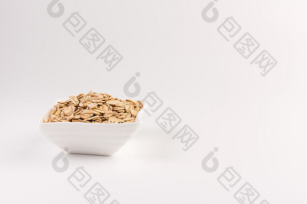 在白色背景上分离的碗中的干滚燕麦。