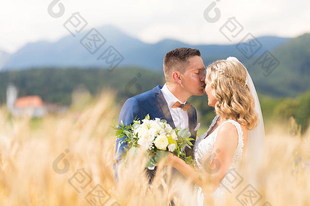 在斯洛文尼亚农村的麦田里，新郎温柔地拥抱新娘，亲吻她的额头。白种人幸福浪漫的年轻夫妇名人