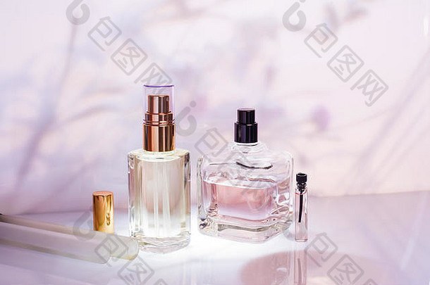 粉红色花朵背景上的不同香水瓶和采样器。化妆品