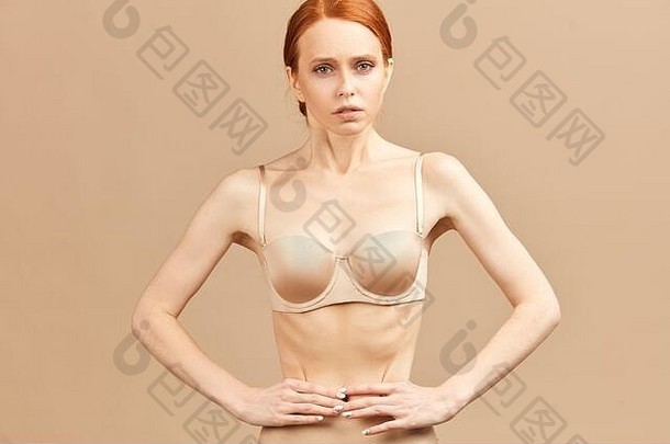 一位穿着内衣的瘦女人用卷尺绑着腰，摆出厌食和饮食失调的姿势