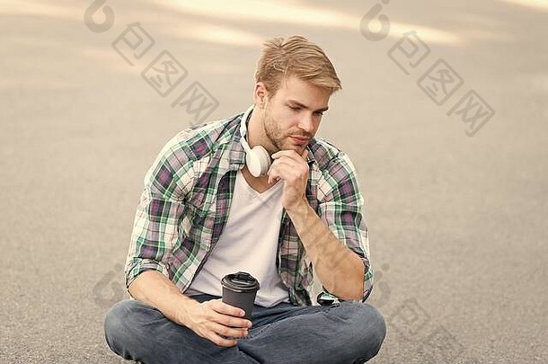 咖啡咖啡的家伙喝咖啡户外男人。坐地面累了学生耳机在线教育听音乐电子书概念男人。网纹衬衫学生放松充电