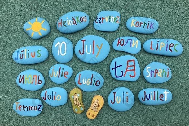 7月10日，绿色沙滩上彩色石头上的多种语言日历日期