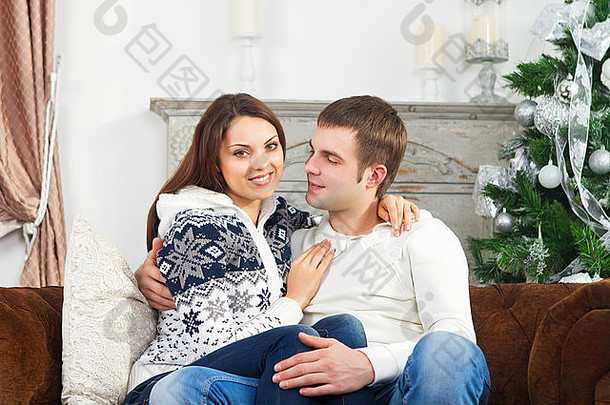 年轻的快乐夫妇坐着沙发圣诞节树