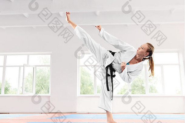 穿着白色和服和黑带表演武术的年轻活跃的女孩高踢腿技巧。运动型空手道女子在搏击课上提高对抗大窗口的技术。体育的概念。