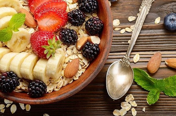 在木制厨房桌子上的粘土盘中，可以俯瞰水果健康的慕斯丽，香蕉、草莓、杏仁和黑莓