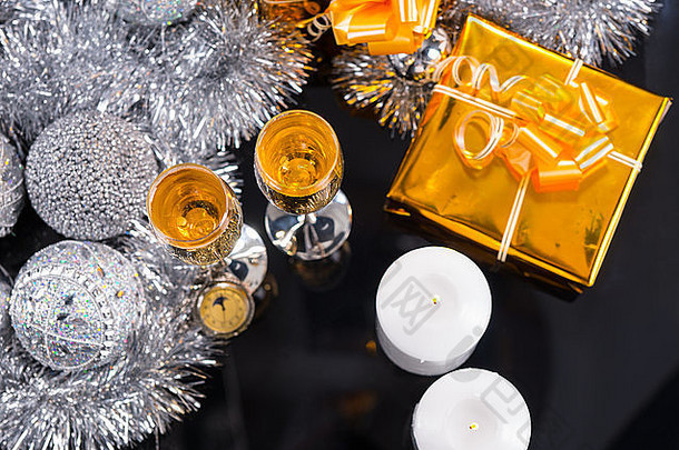 高角度节日圣诞静物画-怀表、香槟酒杯、两支点燃的蜡烛和用金纸包裹的礼物，还有银色金属花环和装饰球。