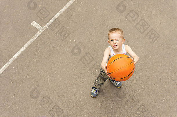 从上面看，一个可爱的小男孩正把篮球对准球网，脸上带着专注的表情