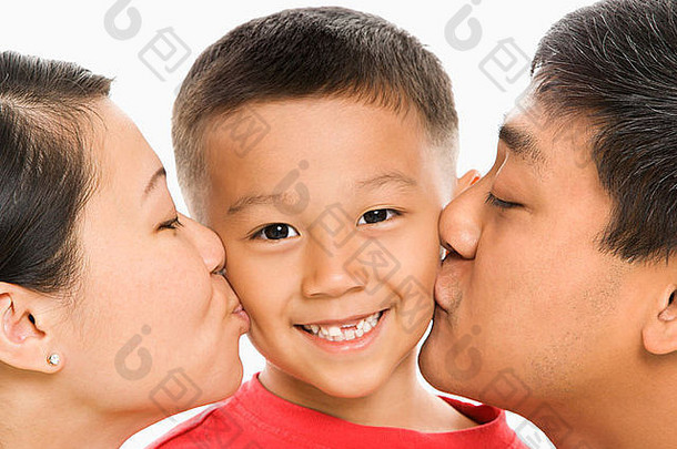 亚洲父母在白色背景前亲吻微笑着的儿子对面的脸颊