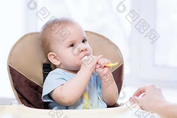 小孩坐在椅子上用勺子吃饭