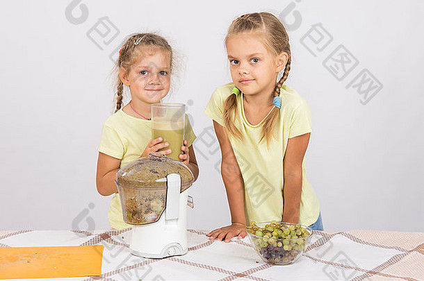 桌上的两个女孩用榨汁机从梨和葡萄中榨汁