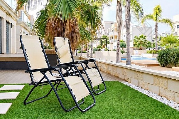 西班牙，私人区后院住宅避暑别墅内人造草坪上的两张躺椅，可观赏带游泳池的现代住宅