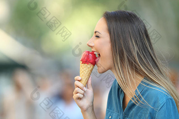 一个快乐的女人在街上咬冰淇淋的侧视图