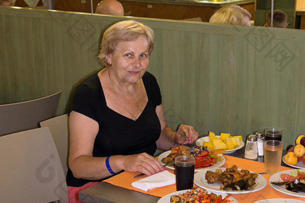 面带微笑的老太太正坐在桌旁，端着许多美味的菜肴。