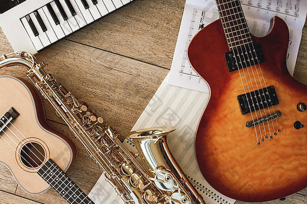 不同乐器的组合：合成器、电子吉他、萨克斯管和四弦琴、铺有音符的床单和木地板。乐器。音乐设备