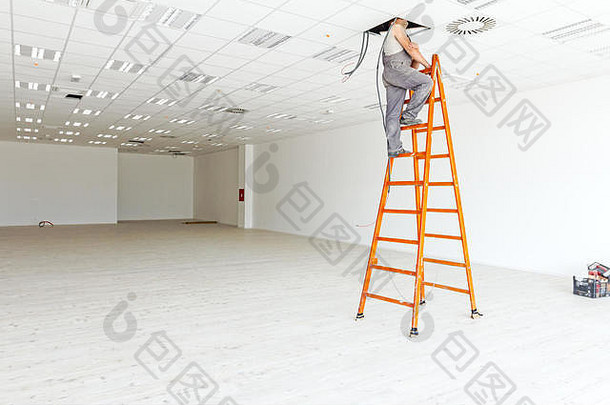 电工站在梯子上，透过天花板上的一个洞窥视着一个白色的、空荡荡的大展厅，展厅的地板是硬木的，地板是f