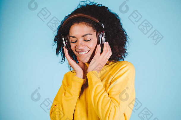 生活方式概念。美丽的非洲裔美国妇女在手机上快乐地听音乐的肖像。蓝色粉彩工作室背景。空间。