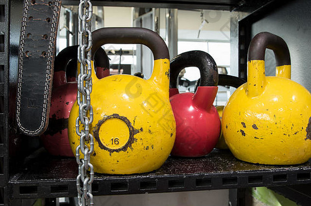 一套五颜六色的破旧<strong>壶</strong>铃放在健身房的金属架子上。