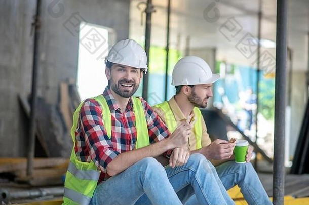 建筑工人黄色的背心头盔坐着咖啡三明治笑