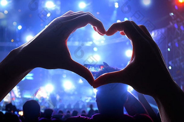 现场音乐会上，一双心形的手和一群观众的剪影，灯光照亮了音乐会的力量