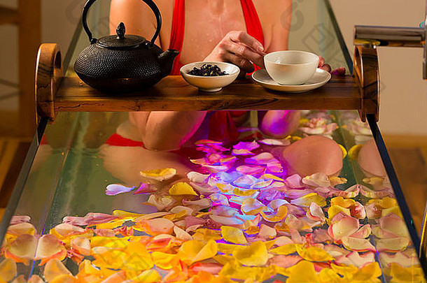 在水疗中心用色彩疗法洗澡的女人，浴缸里有五颜六色的灯光，浴缸上有许多花瓣和茶