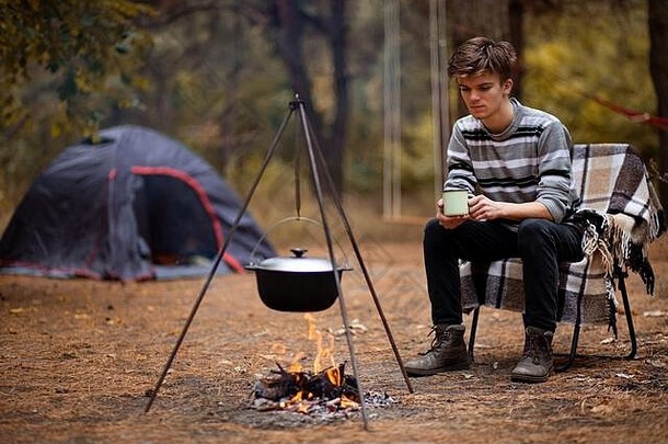 秋天的一天，年轻人在帐篷里露营，在篝火上做饭。度假理念